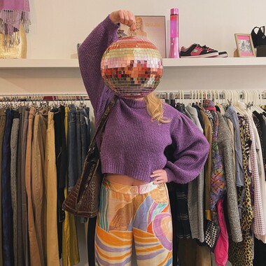 Une personne vêtue d'un pull violet, tenant une boule à facette dans le magasin