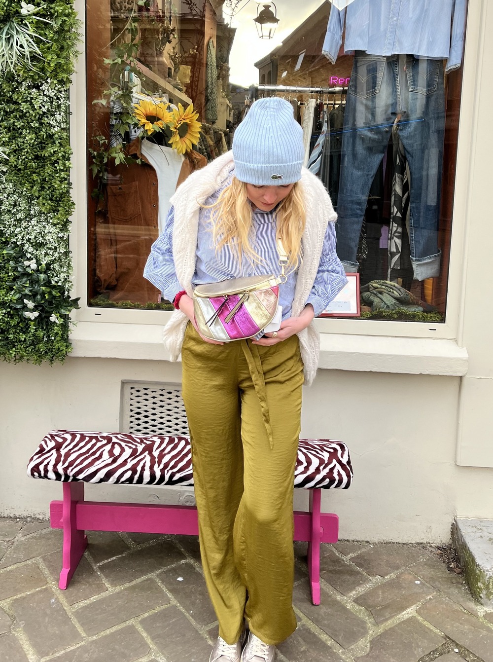 Une femme avec un bonnet et une chemise bleue, un pantalon kaki et un sac coloré de rose et de beige